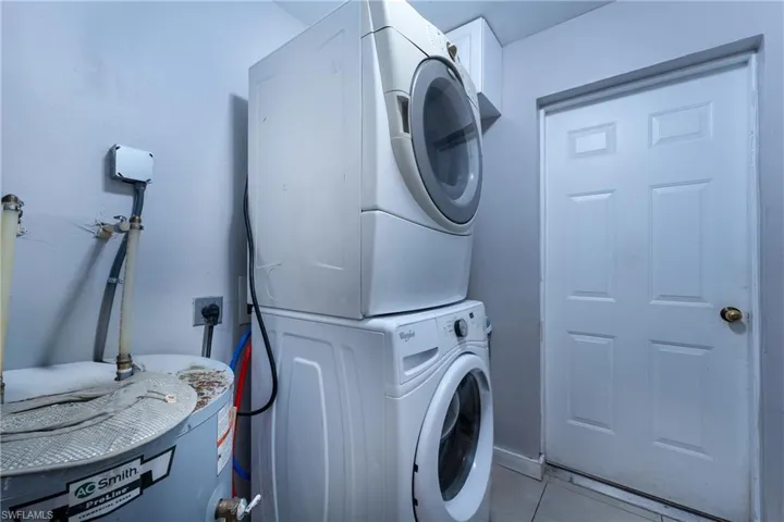 Laundry room with stacked washer and clothes dryer, water heater, light tile floors, and electric dryer hookup