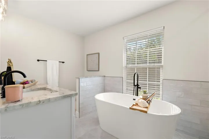 Master bath featuring tile walls, a soaking tub, vanity, and tile floors