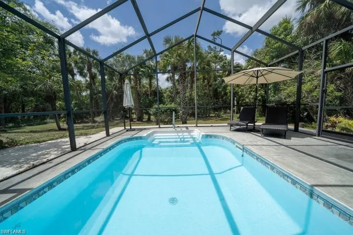 Swimming pool with glass enclosure, a patio area, and view of scattered trees