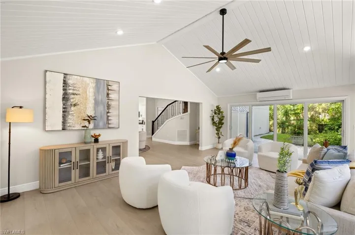Living room featuring an AC wall unit, stairs, a ceiling fan, light wood-type flooring, and high vaulted ceiling