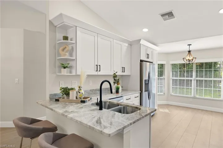 Kitchen with stainless steel fridge, open shelves, white cabinets, light stone countertops, and hanging light fixtures