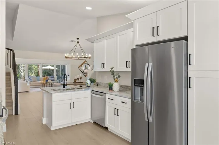 Kitchen with stainless steel appliances, a peninsula, open floor plan, white cabinetry, and a chandelier