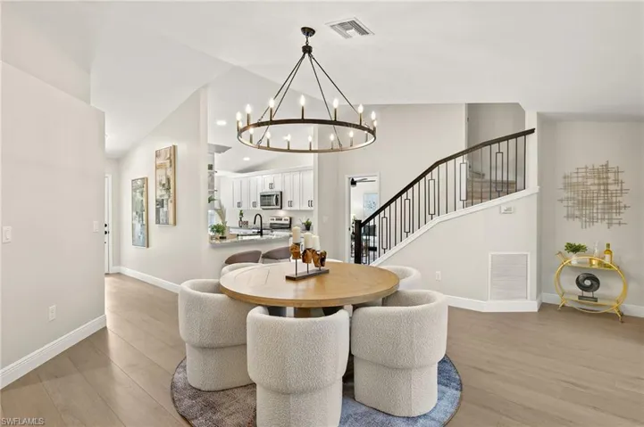 Dining space with light wood-style flooring, a chandelier, stairs, and high vaulted ceiling