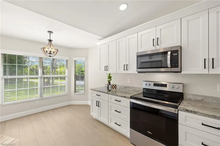 Kitchen with stainless steel appliances, lofted ceiling, white cabinets, hanging light fixtures, and a chandelier