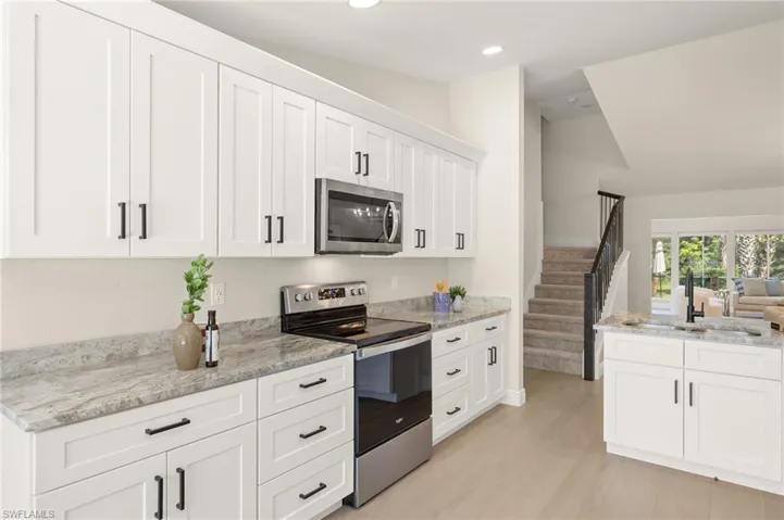 Kitchen with appliances with stainless steel finishes, white cabinets, light wood-style floors, light stone countertops, and recessed lighting