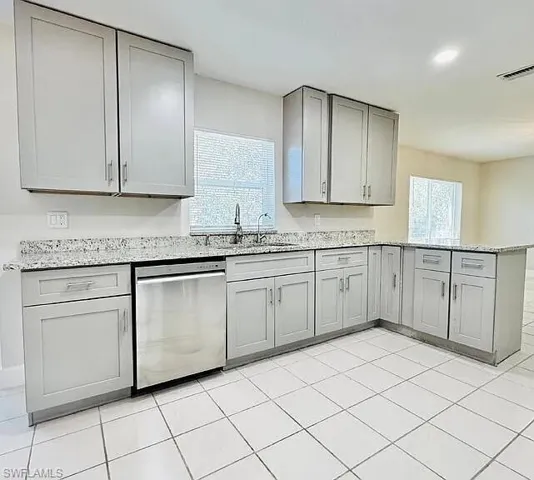 L-shaped kitchen with light gray cabinetry, stainless steel dishwasher, speckled countertops, and white tile flooring