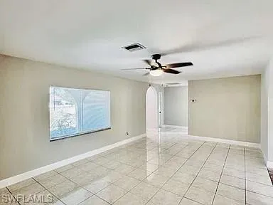 Neutral toned walls, tile flooring, ceiling fan with integrated lighting, and an arched doorway