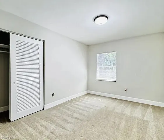 Light-colored wall-to-wall carpeting, white baseboards, and a single window with blinds