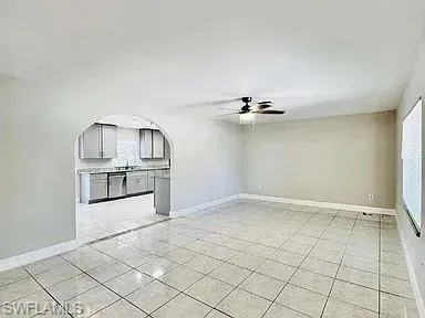 Tiled flooring throughout, ceiling fan with integrated lighting, window with blinds, arched entryway, and kitchen with gray cabinetry and countertops