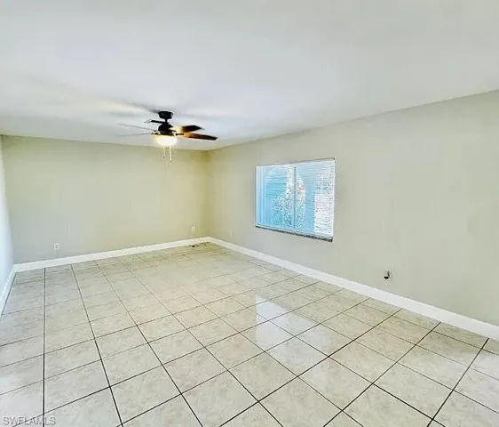 Spacious room featuring tile flooring, neutral wall tones, a ceiling fan with integrated lighting, and a single window with blinds