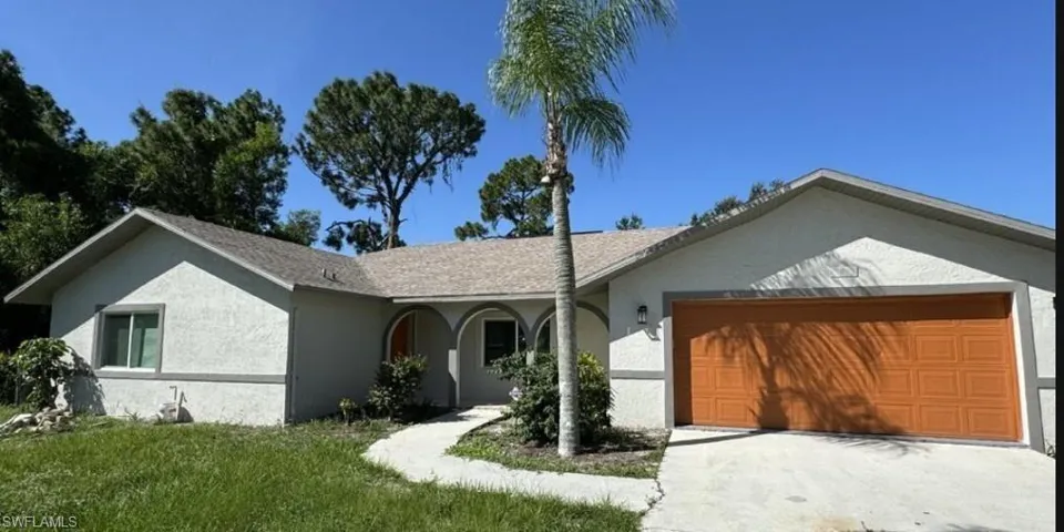 Stucco exterior with a tan-toned garage door, arched entryway, and a curved concrete pathway