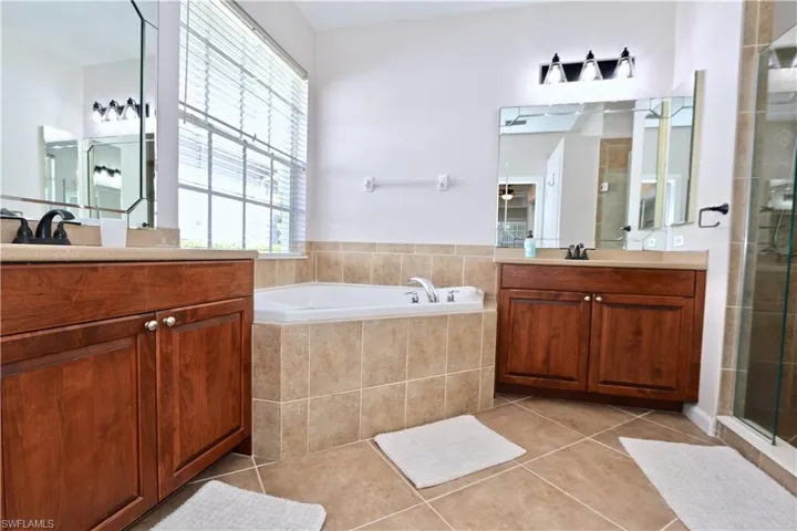 Bathroom featuring a corner soaking tub, dual wood-finish vanities with light countertops, and a tiled shower enclosure