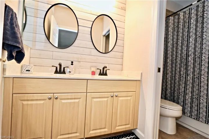 Double vanity with light wood-finish cabinetry and quartz-finish countertop