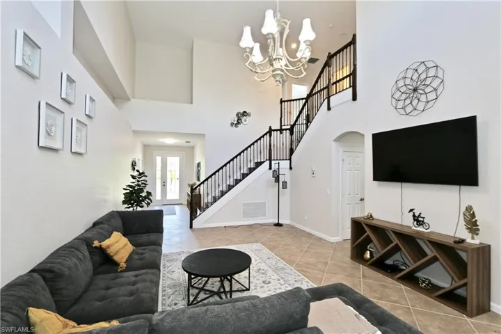Spacious two-story living area featuring high ceilings, a grand staircase with dark wood railings, and tile flooring
