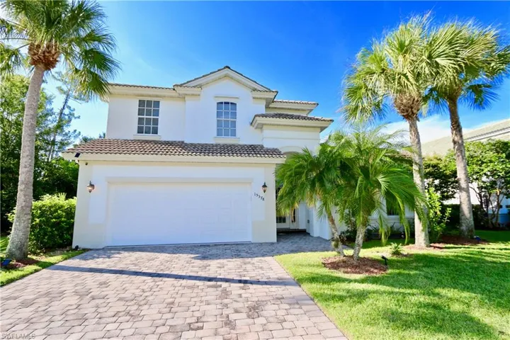 Stucco exterior with a two-car garage, tile roof, and a paver driveway