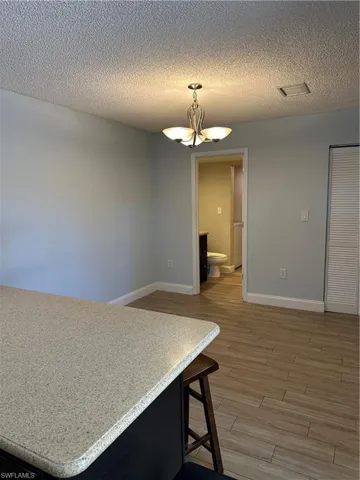 Unfurnished dining area with light wood finished floors, a chandelier, baseboards, and a textured ceiling