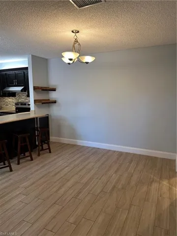 Dining space with light wood-style floors, a textured ceiling, baseboards, and a chandelier