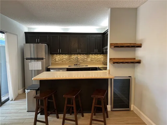 Kitchen featuring beverage cooler, a sink, light countertops, a breakfast bar area, and decorative backsplash