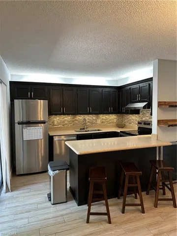 Kitchen with refrigerator, range, dark cabinetry, a sink, and a textured ceiling