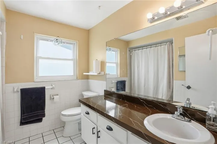 Full bathroom with vanity, curtained shower, light tile patterned floors, tile walls, and a wainscoted wall