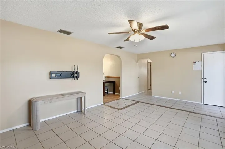 Spare room with light tile patterned floors, ceiling fan, arched walkways, and a textured ceiling