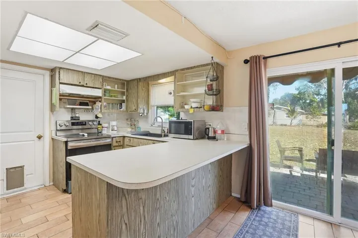 Kitchen with stainless steel appliances, a peninsula, light countertops, backsplash, and open shelves