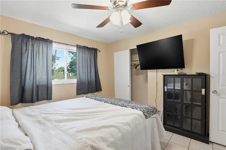 Bedroom featuring a textured ceiling, light tile patterned floors, a closet, and a ceiling fan