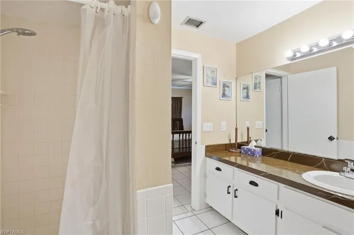 Ensuite bathroom featuring vanity, light tile patterned floors, and a tile shower