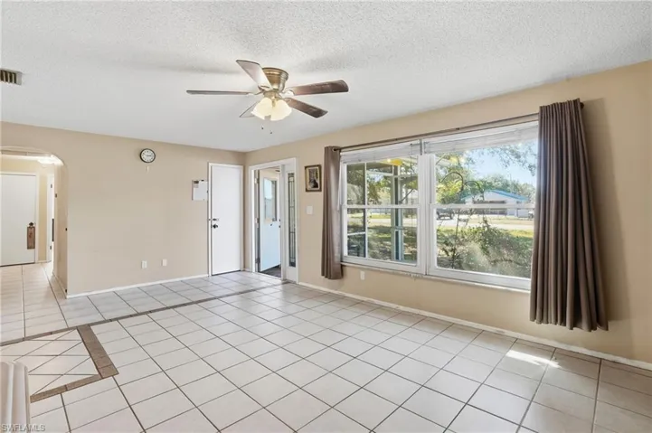 Empty room with arched walkways, ceiling fan, light tile patterned floors, and a textured ceiling