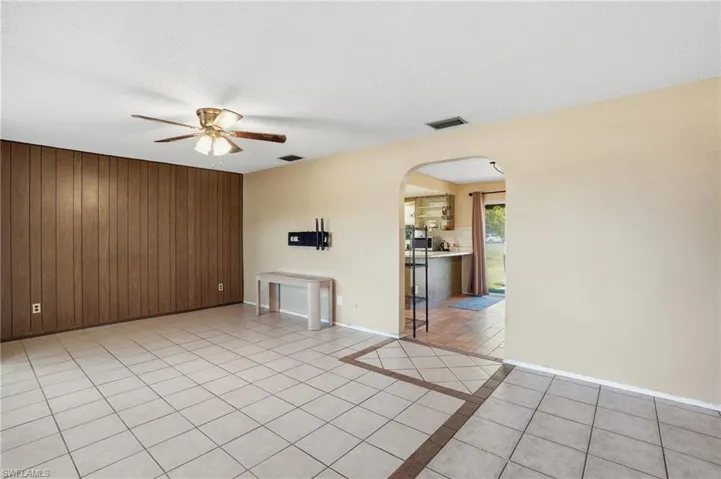 Unfurnished living room with wood walls, arched walkways, a ceiling fan, light tile patterned floors, and a textured ceiling
