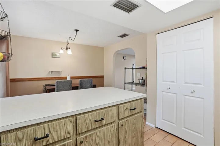 Kitchen with light countertops, arched walkways, light wood finish cabinetry, and pendant lighting