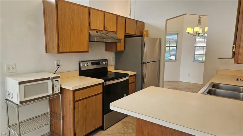 Kitchen with sink, light tile patterned floors, pendant lighting, a notable chandelier, and appliances with stainless steel finishes