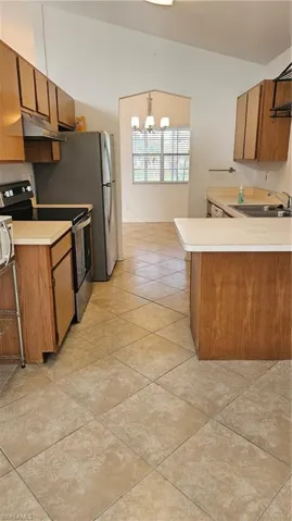 Kitchen with a chandelier, kitchen peninsula, decorative light fixtures, stove, and exhaust hood