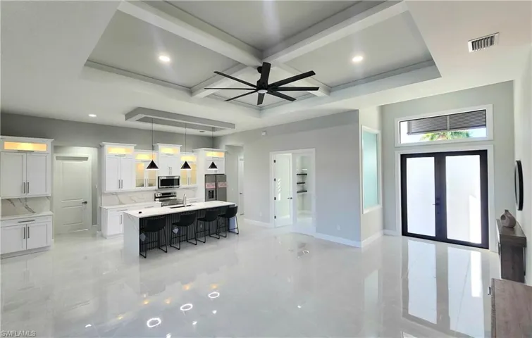 Kitchen featuring coffered ceiling, white cabinetry, glass insert cabinets, an island with sink, and a breakfast bar area