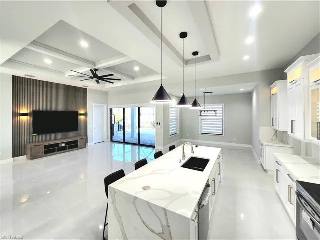 Kitchen with open floor plan, light stone countertops, a kitchen breakfast bar, white cabinets, and a spacious island