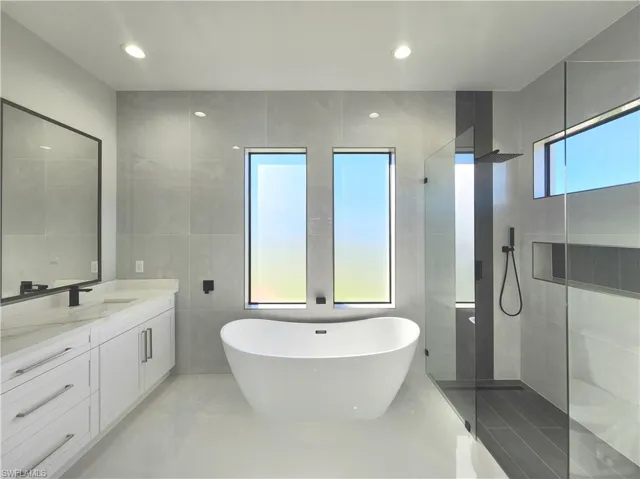 Full bathroom featuring walk in shower, a freestanding tub, vanity, recessed lighting, and tile walls