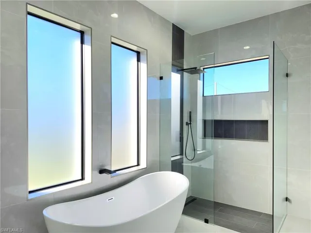 Full bath featuring a walk in shower, a freestanding tub, and tile walls
