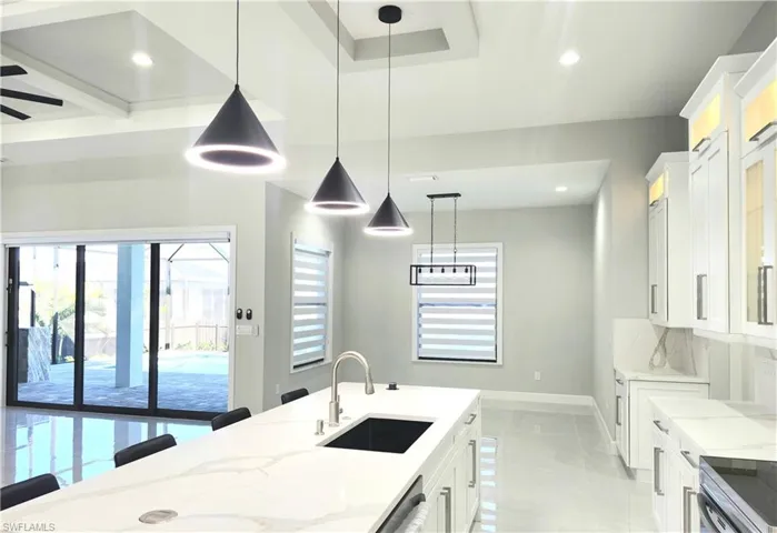 Kitchen featuring light stone counters, a kitchen bar, hanging light fixtures, white cabinets, and glass insert cabinets