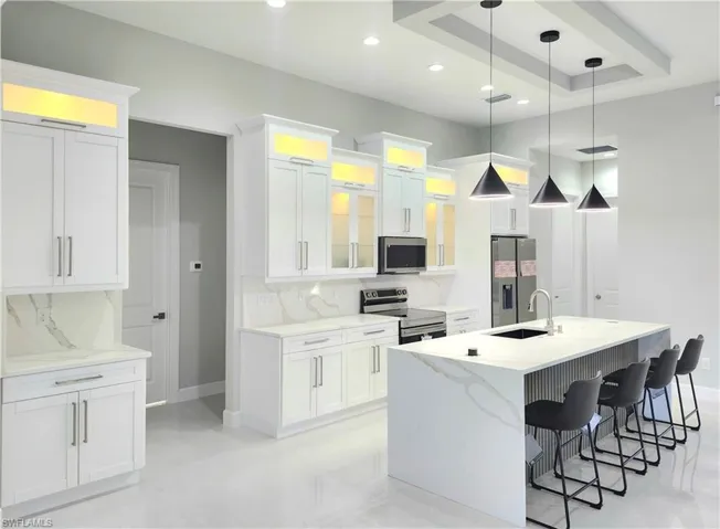 Kitchen featuring stainless steel appliances, decorative light fixtures, white cabinets, backsplash, and light stone countertops