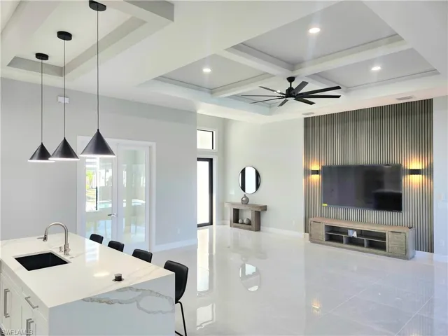 Kitchen featuring a kitchen breakfast bar, decorative light fixtures, light stone counters, coffered ceiling, and a center island with sink