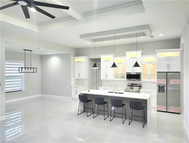 Kitchen featuring appliances with stainless steel finishes, a breakfast bar, light stone countertops, a kitchen island with sink, and pendant lighting