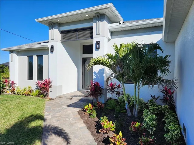 View of exterior entry with stucco siding, a lawn, and a shingled roof