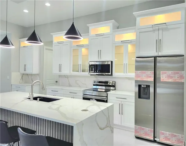 Kitchen with stainless steel appliances, white cabinetry, light stone counters, glass insert cabinets, and decorative light fixtures