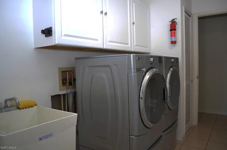 Laundry area with tile patterned flooring, separate washer and dryer, cabinets, and sink