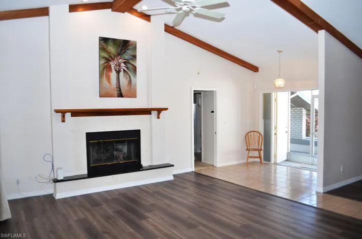 Unfurnished living room featuring wood-type flooring, lofted ceiling with beams, and ceiling fan
