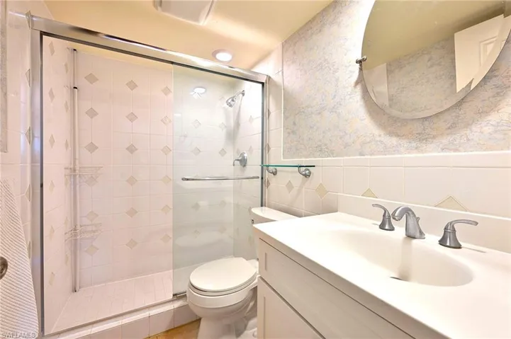 Bathroom with vanity, a shower with door, tile walls, and toilet