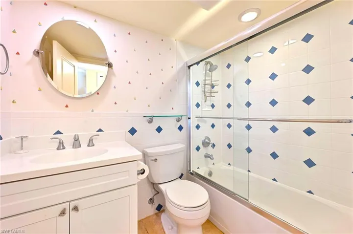 Full bathroom with shower / bath combination with glass door, tile walls, vanity, tile patterned floors, and toilet