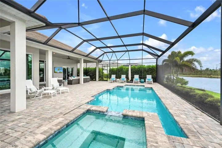 View of swimming pool with ceiling fan, glass enclosure, a patio, an in ground hot tub, and a water view.