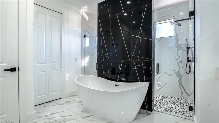 Bathroom featuring a closet, a freestanding tub, a marble finish shower, and light marble finish flooring