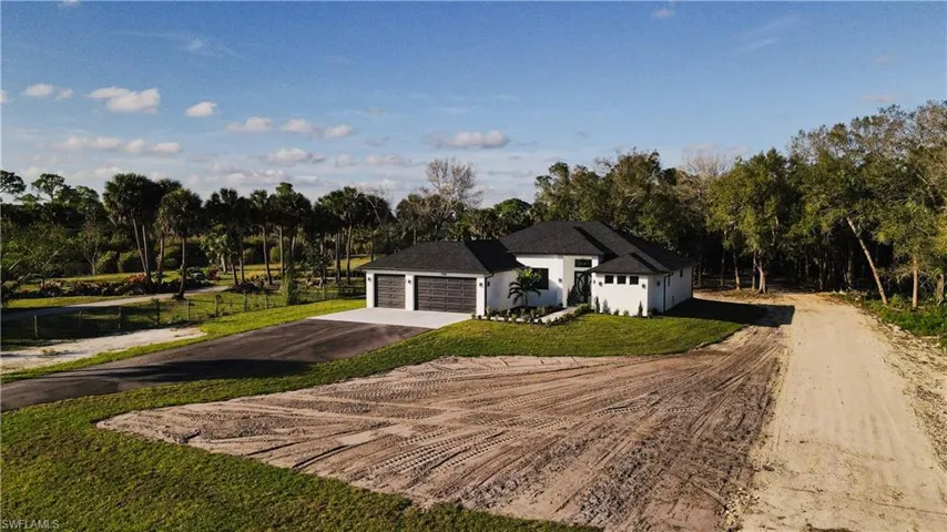 View of front of house featuring dirt driveway, stucco siding, and view of wooded area
